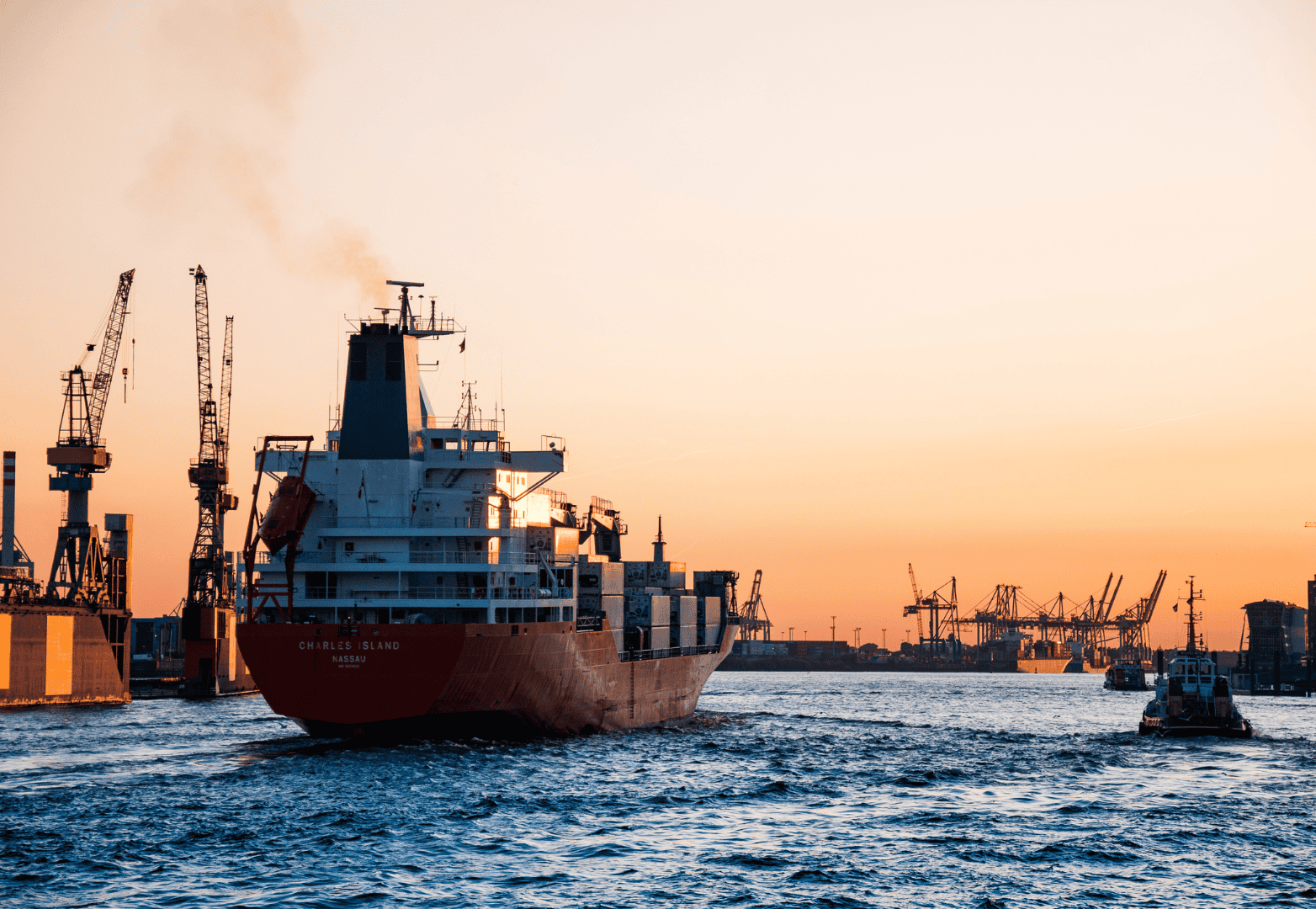 Cargo ship docked at port during sunset with cranes in the background, illustrating maritime logistics and shipping industry.