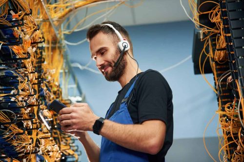 Close-up of a technician using mobile device amidst network cables in data center.